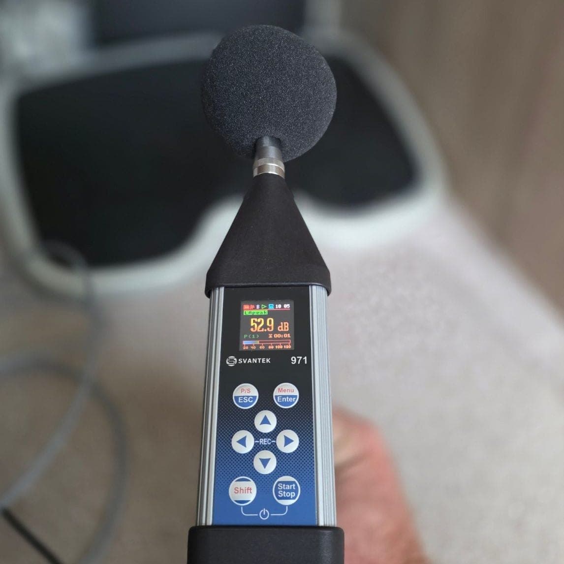 Close-up van een Svantek 971 klasse-1 geluidsmeter met een zwarte windkap op de microfoon. Het display toont 52,9 dB met het label LApeak.